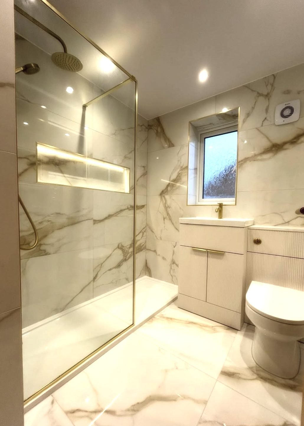Marble effect bathroom with brushed brass walk-in shower screen and lit niche